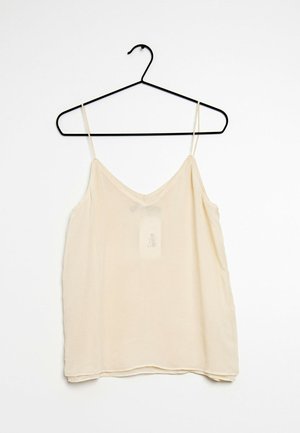 Lichtbeige mouwloze camisole met dunne bandjes, V-hals, iets doorzichtige stof en een zichtbaar etiket aan de voorkant. Hangt aan een zwarte haak.
