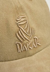 Beżowa czapka z teksturowanej tkaniny z haftowanym logo "DAKAR" w kolorze brązowym. Projekt obejmuje zakrzywiony daszek oraz przeszycia na koronie.