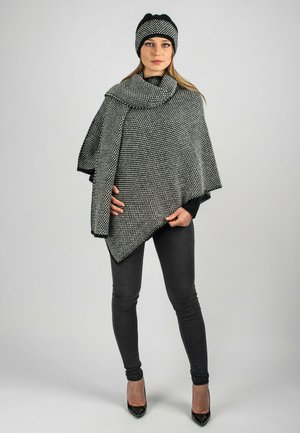 Schwarz-weißer gemusterter Poncho mit passender Mütze, hergestellt aus strukturiertem Stoff. Verfügt über eine asymmetrische Form und fransige Kanten.