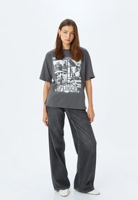 Grijze oversized t-shirt met zwart-wit grafische print, met het woord "PLUGGED." Gecombineerd met losse, donkere spijkerbroeken.
