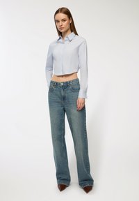 Camicia bottonata azzurra chiara a maniche lunghe, abbinata a jeans di denim blu medio a vita alta e gamba larga, con tacchi appuntiti marroni.