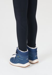 Blå ankelstøvler med en struktureret overflade, hvidt faux-fur for og brune gummisåler. Båret med sorte leggings.