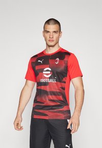 Camiseta de fútbol de manga corta en rojo y negro con un patrón texturizado, que presenta un cuello redondo y un logo en el pecho.