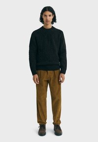 Suéter de punto negro, pantalones de pana marrones con rayas verticales y zapatos marrones. Diseño simple y corte relajado en toda la prenda.