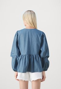 Zila svītrainā pepluma blūze ar pūkainām piedurknēm, izgatavota no denima. Iespējo brīvu piegriezumu un apaļu kakla izgriezumu. Saskaņota ar baltām izsistām šortiem.