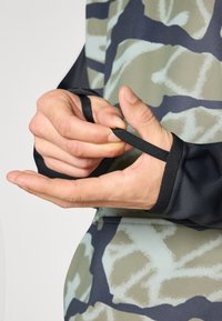 Garšīgām piedurknēm kreklam ar melnu un nomāktu kamuflāžas rakstu, kura priekšrocība ir pirkstu caurumi piedurknēs un gluda, stiepjas auduma tekstūra.
