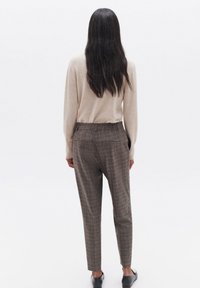 Beiger Pullover und braune Karo-Hosen, taillierte Passform, mit Schlitztaschen und umgeschlagenem Saum. Glatte Textur, minimalistisches Design und dunkle Schuhe.