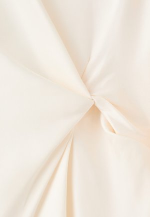 Material de culoare crem răsucit în centru, arătând o textură netedă și pliuri moi care radiază spre exterior.