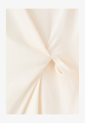 Material de culoare crem răsucit în centru, arătând o textură netedă și pliuri moi care radiază spre exterior.