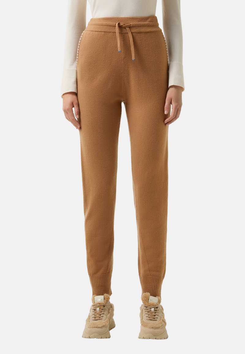 Braune Jogginghosen aus weichem Material, mit einem Kordelzug in der Taille, gerippten Bündchen und dezenten seitlichen Details. Getragen mit beigen Turnschuhen.