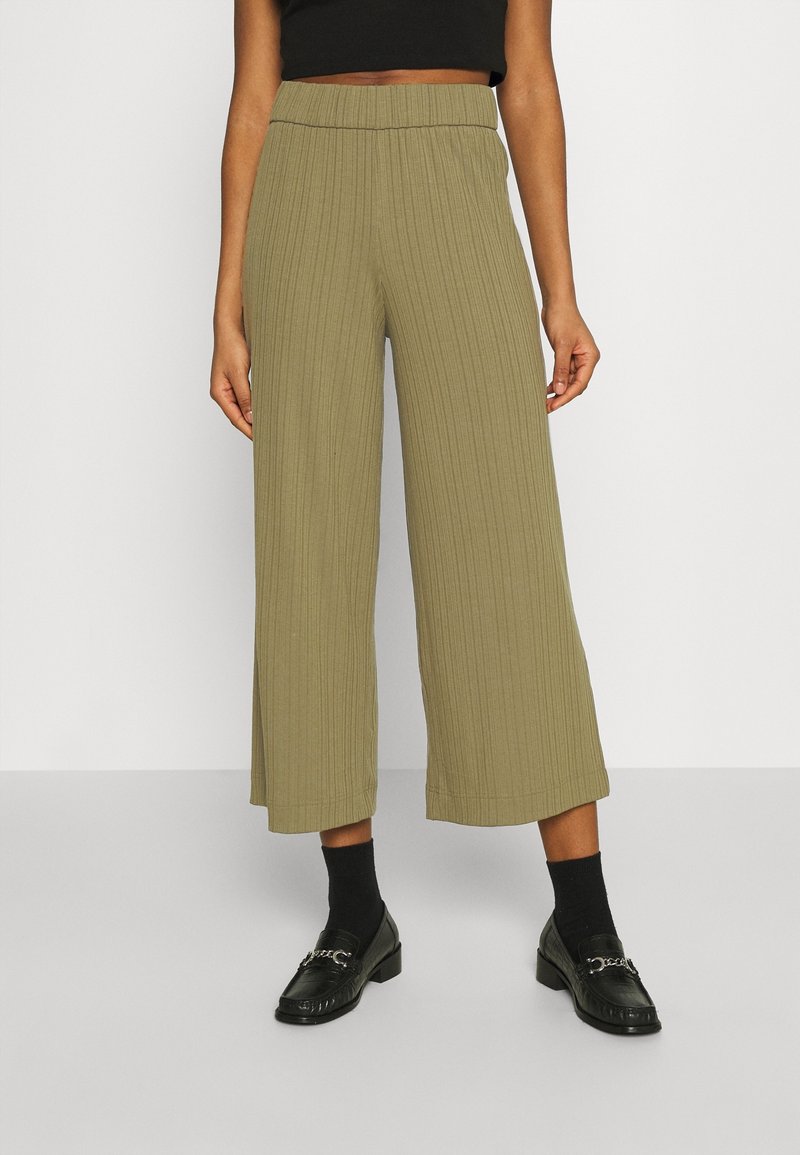 Pantalon large kaki avec texture côtelée verticale, taille haute élastique, longueur raccourcie, assorti à des mocassins noirs et des chaussettes.