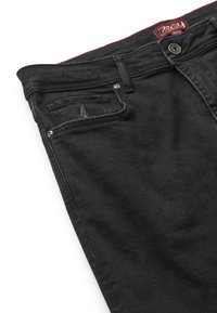 Jeans negri din denim, pliați pentru a arăta partea superioară frontală cu bucle pentru curea, nasture, buzunar pentru monede și etichetă de brand roșie în interiorul taliei.