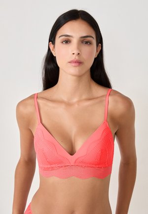 Bralette rose corail avec un motif en dentelle ondulée, bretelles ajustables et décolleté plongeant. Texture douce et design sans couture.