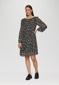 Robe à motifs floraux noir et blanc avec de longues manches bouffantes et un col rond ; portée avec des mocassins noirs brillants.