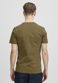 Tricou scurt cu mânecă, de culoare verde măsliniu, realizat din bumbac, cu guler rotund și o croială dreaptă, având o textură netedă și detalii minime.