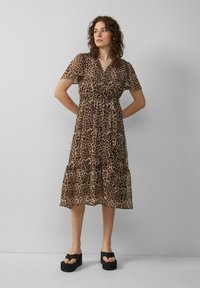 Jurkend met luipaardprint in doorschijnende stof, met korte mouwen, een wikkelontwerp, een gelaagde rok en een middellange snit. Zwarte plateau-sandalen maken de look compleet.