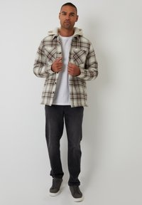 Koszula w kratę flanelowa w kolorze kremowym, brązowym i czarnym z kapturem; posiada dwie kieszenie na piersi i zapięcie na guziki. Połączona z szarymi spodniami i trampkami.