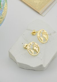 Guldörhängen formade som en glob med utskurna kontinenter. De är placerade på en strukturerad vit stenyta.