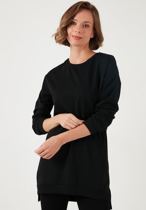Black long-sleeve tunic made of soft fabric, featuring a round neckline, relaxed fit, and side slits at the hem for ease of movement.