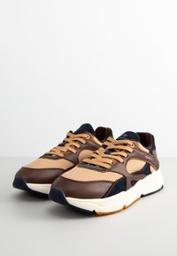 Brown and beige sneakers with mesh and leather materials, featuring navy accents, round toe, and thick white outsole with textured grip.
