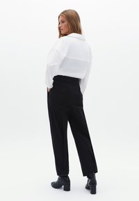 Camicia bianca semi-trasparente con colletto e maniche lunghe. Pantaloni neri sartoriali con tasche laterali e vestibilità affusolata. Stivali neri con tacco.