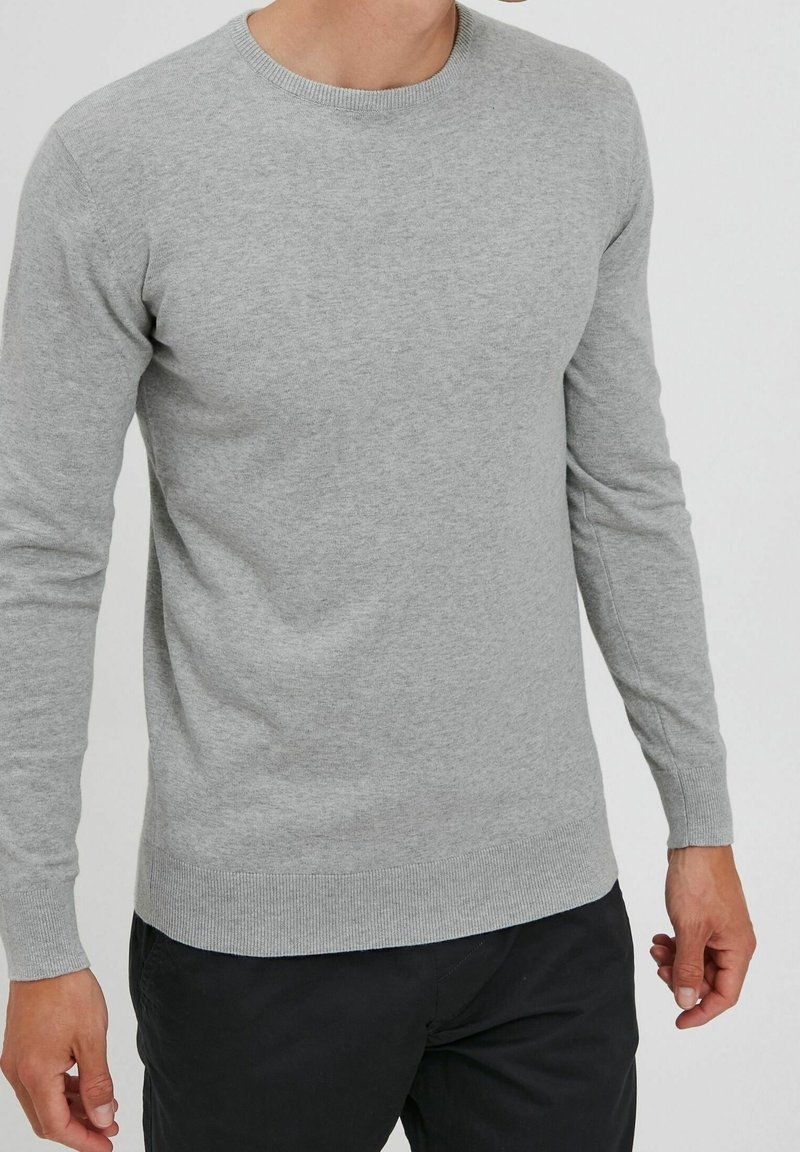 Maglione grigio lavorato a maglia con scollatura tonda e maniche lunghe. Presenta polsini e orlo a costine, evidenziando una morbida texture e un design aderente.