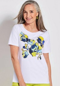 Helles T-Shirt mit kurzen Ärmeln in Weiß, verziert mit einem blauen und gelben Blumenmuster und glitzernden Akzenten. Rundhalsausschnitt und weiche Textur.