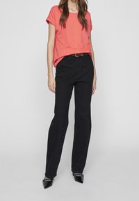 Korálové tričko s krátkým rukávem, volný střih, v kombinaci s černými džíny rovného střihu a černými špičatými lodičkami. Minimalistický design bez vzorů.