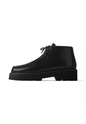 Bottine noire en cuir avec semelle épaisse et laçage à l'avant, vue de profil sur fond blanc.