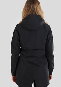 Chaqueta impermeable negra con cintura ajustada, capucha y una abertura en la parte posterior, con una textura lisa y un diseño aerodinámico.