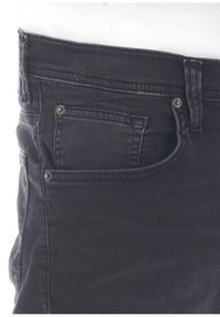 Jeans in denim nero con un classico design a cinque tasche, leggeri segni di usura e dettagli in metallo. Il tessuto ha una texture liscia.