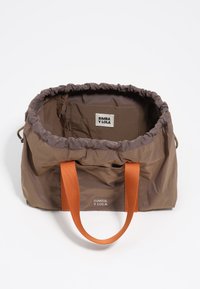 Bolso tote de nylon marrón con parte superior fruncida. Presenta asas de tela naranja y una etiqueta en el interior con "BIMBA Y LOLA" impresa.