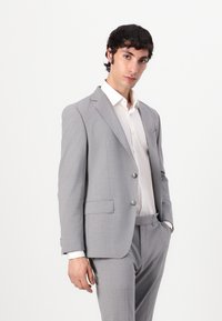 Light grey suit made of a textured fabric, featuring a single-breasted jacket with two buttons and matching trousers, paired with a white shirt.