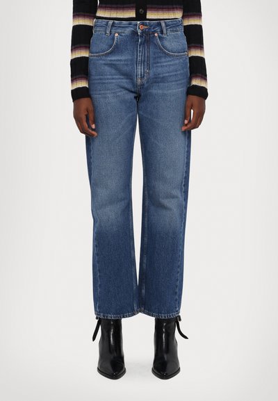 High-waisted, wide-leg blue denim jeans with a clean finish, five pockets, and copper hardware details, paired with black pointed ankle boots.