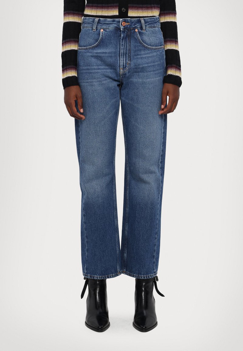 Jeans din denim albastru, cu talie înaltă și picătură largă, cu un finisaj curat, cinci buzunare și detalii din hardware cupru, asortați cu cizme negre cu vârf ascu�țit.