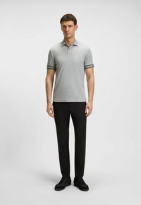 Polo grigia con colletto, maniche corte con righe nere. Accompagnata da pantaloni neri e sneakers nere per un look casual.