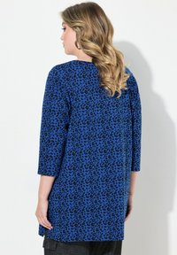 Top blu con stampa leopardata nera, maniche a tre quarti e vestibilità rilassata. Il tessuto appare liscio con una leggera lucentezza.