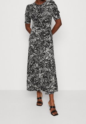 Vrouw draagt een midi-jurk met een zwart-wit abstract swirl-patroon, korte mouwen en zwarte sandalen met hak.