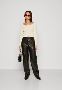 Off-white langermet topp med teksturert stoff, parret med høyt liv sorte skinnbukser. Tilbehøret inkluderer røde solbriller og en liten veske.