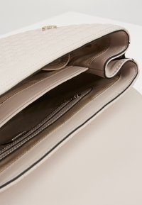 Jasnoróżowa pikowana torebka z zapięciem na złoty guzik, wieloma przegródkami i kieszenią na zamek. Gładka podszewka wewnętrzna oraz czarne akcenty.