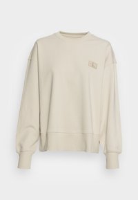 Beige sweatshirt med rund halsringning, nedhasade axelsömmar, ribbade muddar och nederkant. Har en liten präglad logotyp på övre vänstra sidan.