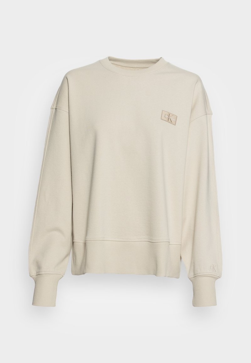 Beige sweatshirt med rund halsringning, nedhasade axelsömmar, ribbade muddar och nederkant. Har en liten präglad logotyp på övre vänstra sidan.