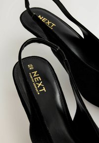 Pantofi slingback din catifea neagră cu vârf ascuțit, curele subțiri și o branță neagră netedă, având detalii de text în aur și mărimea.