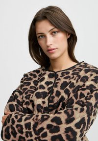 Giacca con stampa leopardata in beige e nero, con collo rotondo, chiusura a bottoni e tessuto morbido con una finitura leggermente testurizzata.