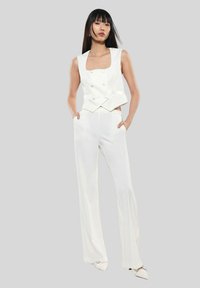 Gilet bianco su misura con scollatura quadrata e bottoni doppi, abbinato a pantaloni bianchi a gamba larga. Design liscio e minimalista.