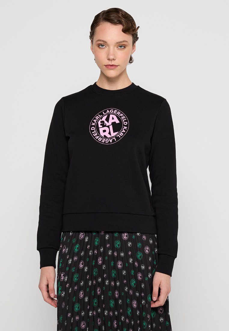 Sudadera negra de algodón, con un logo rosa redondo en el pecho. Manga larga y puños de canalé con un ajuste clásico.