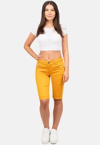 Gele katoenen bermuda shorts met voorzakken en contrasterende stiksels, gecombineerd met een getailleerd wit cropped t-shirt en witte sneakers.