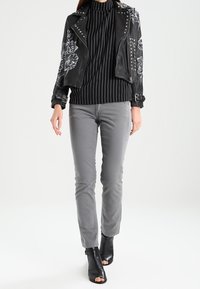 Chaqueta de cuero negra corta con bordados florales y tachuelas, combinada con una blusa de rayas en blanco y negro y pantalones grises. Botines negros con punta abierta.