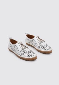 Zapatos blancos con cordones, con patrones florales recortados, interior en tono marrón y suela tipo corcho. Punta redondeada y diseño plano. Superficie superior texturizada.