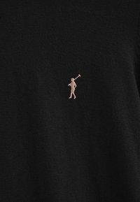 Czarny sweter z dzianiny z małym różowym haftowanym logo przedstawiającym postać trzymającą kij do golfa. Miękka tekstura i klasyczny, swobodny fason.